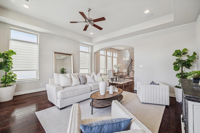 living area with dark wood-type flooring, baseboards, recessed lighting, arched walkways, and a raised ceiling