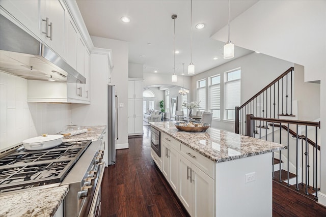 kitchen featuring stainless steel appliances, arched walkways, a kitchen island, and dark wood finished floors