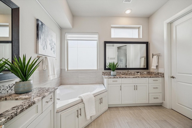 bathroom featuring visible vents, two vanities, a stall shower, a sink, and a bath