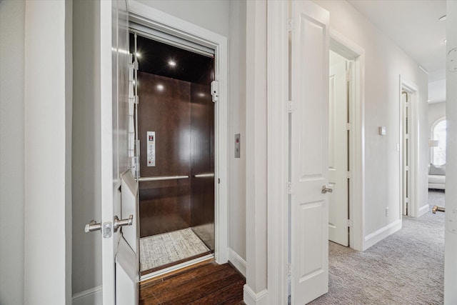 hallway with elevator, baseboards, and carpet floors