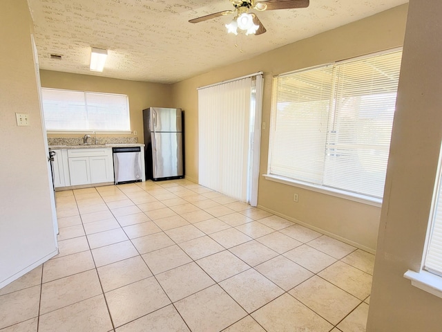 kitchen with a sink, a textured ceiling, appliances with stainless steel finishes, light tile patterned flooring, and white cabinets