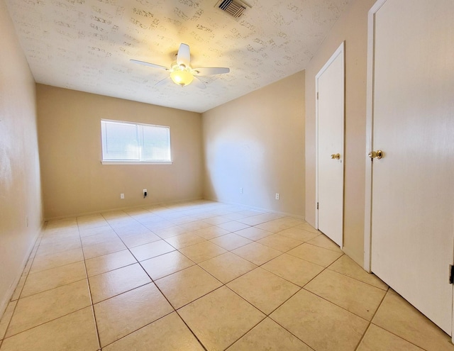 spare room featuring a textured ceiling, light tile patterned flooring, visible vents, and ceiling fan