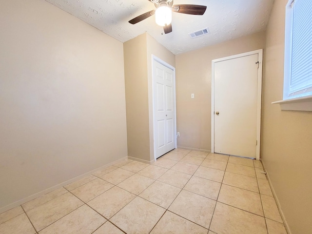 unfurnished bedroom with light tile patterned floors, a ceiling fan, baseboards, visible vents, and a textured ceiling