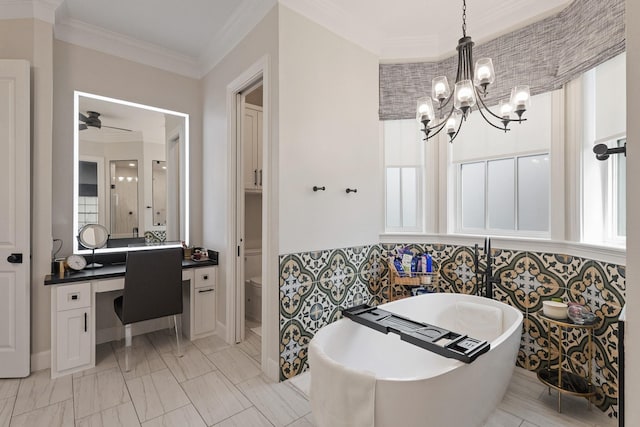 full bathroom featuring vanity, a freestanding bath, ornamental molding, toilet, and ceiling fan with notable chandelier