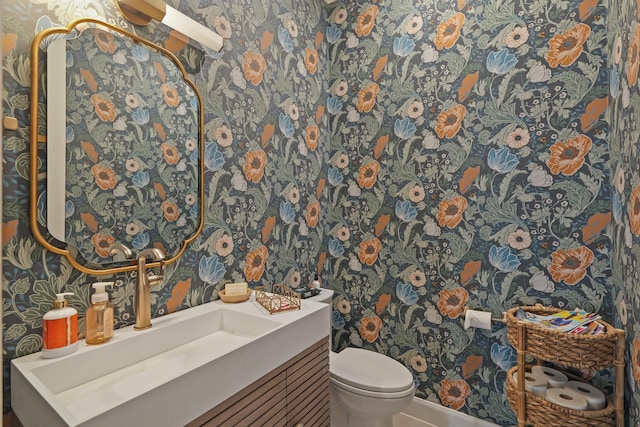 bathroom with toilet, vanity, and wallpapered walls