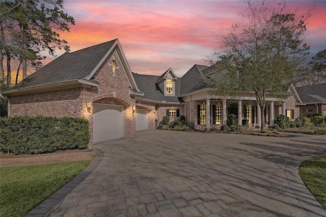 view of front of house featuring brick siding, an attached garage, a shingled roof, and decorative driveway