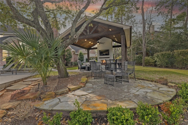 view of patio / terrace with a gazebo, a ceiling fan, and a warm lit fireplace