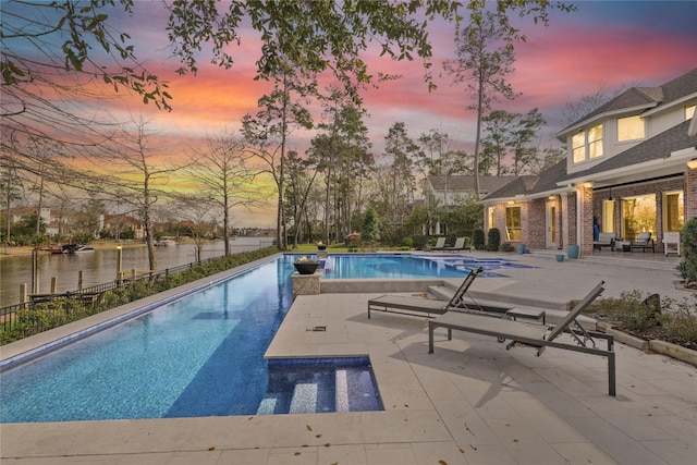 pool at dusk with a patio, a fenced in pool, and a water view