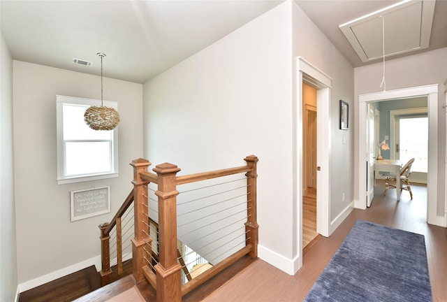 corridor featuring wood finished floors, visible vents, baseboards, attic access, and an upstairs landing