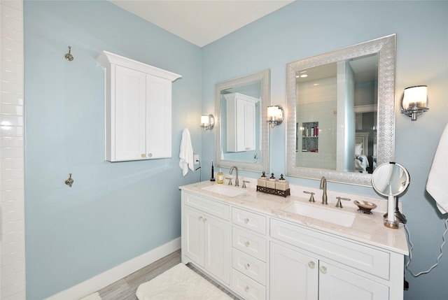 bathroom with double vanity, wood finished floors, baseboards, and a sink