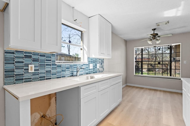 kitchen with visible vents, a sink, white cabinetry, light wood-style floors, and decorative backsplash