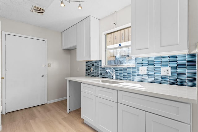 kitchen featuring visible vents, light wood-style flooring, a sink, backsplash, and white cabinets