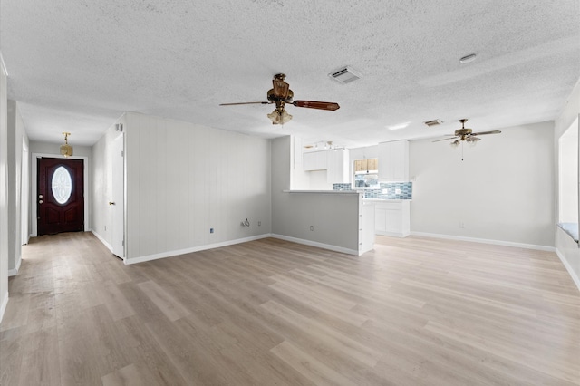 unfurnished living room with light wood finished floors, visible vents, baseboards, a textured ceiling, and a ceiling fan