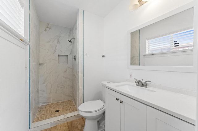 full bathroom featuring a tile shower, toilet, vanity, and wood finished floors