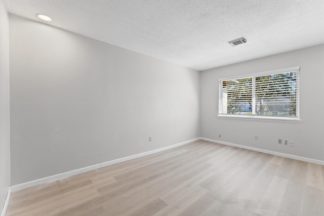 spare room featuring visible vents, light wood-style flooring, a textured ceiling, and baseboards