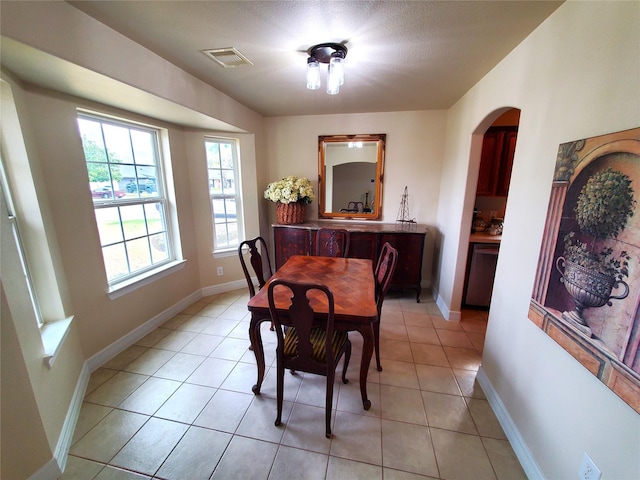 dining space with light tile patterned floors, visible vents, arched walkways, and baseboards