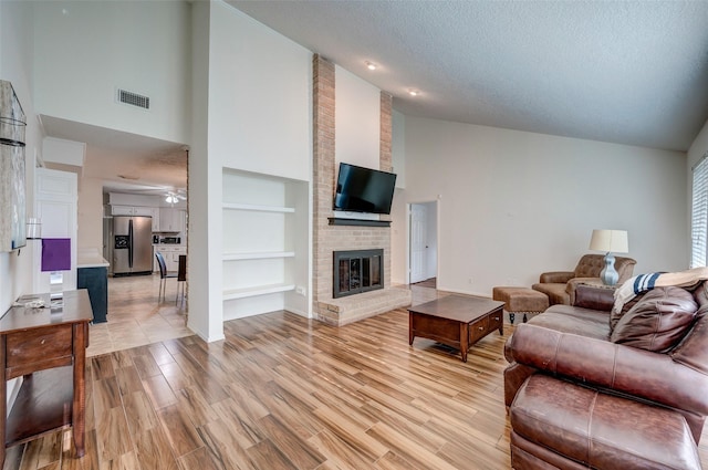 living area with visible vents, built in shelves, a textured ceiling, light wood-style floors, and a fireplace