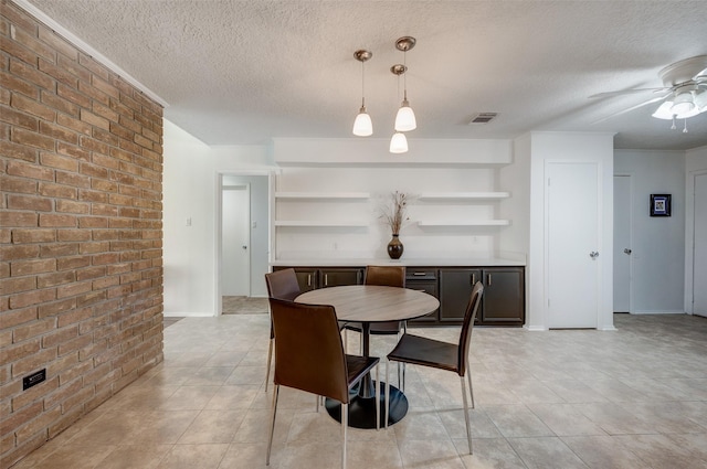 dining area featuring a ceiling fan, visible vents, brick wall, and a textured ceiling