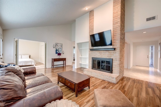 living area featuring visible vents, a brick fireplace, light wood-type flooring, a textured ceiling, and high vaulted ceiling