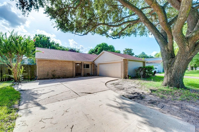 single story home featuring a garage, brick siding, driveway, and fence