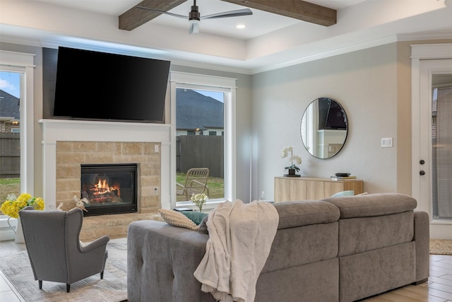 living area featuring light wood-type flooring, beamed ceiling, a stone fireplace, and ceiling fan