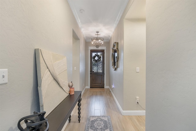 foyer featuring baseboards, ornamental molding, light wood-style flooring, a textured wall, and a notable chandelier