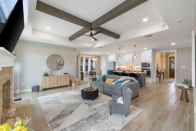 living room with baseboards, visible vents, a fireplace, beamed ceiling, and light wood-type flooring