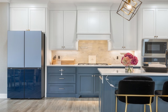 kitchen with blue cabinetry, backsplash, stainless steel appliances, a breakfast bar area, and light countertops