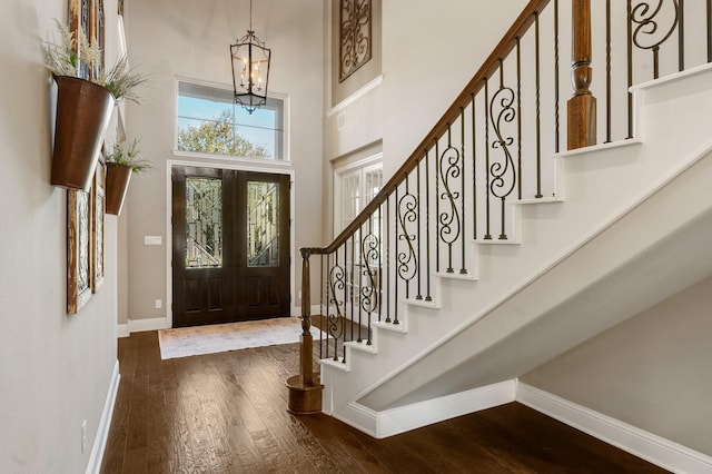 entrance foyer featuring baseboards, dark wood finished floors, stairs, an inviting chandelier, and a towering ceiling