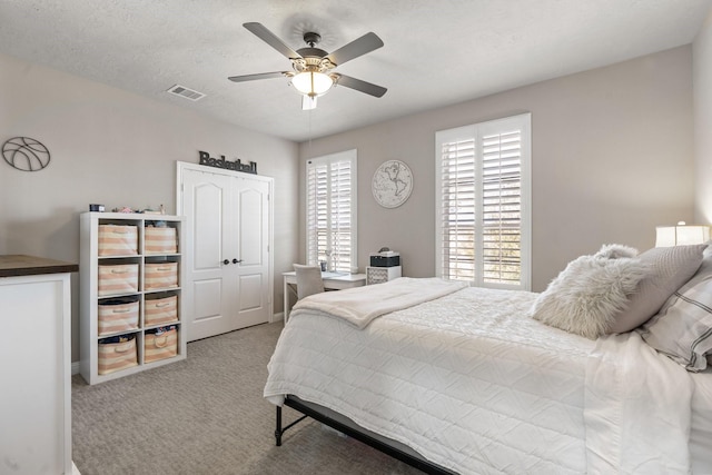 bedroom with light carpet, visible vents, a textured ceiling, and a ceiling fan