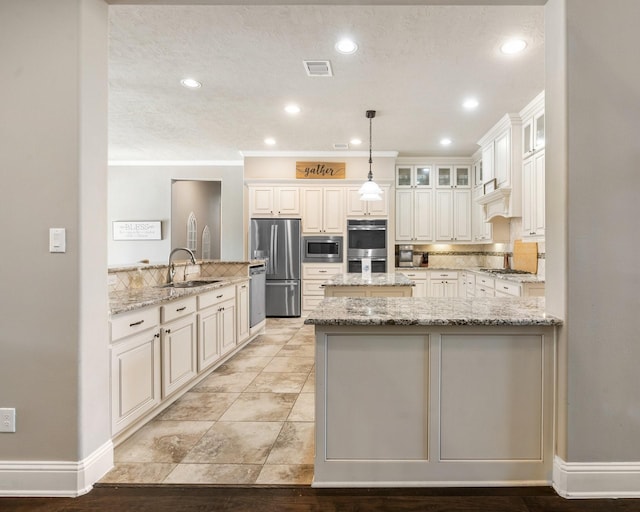 kitchen with light stone counters, a peninsula, a sink, stainless steel appliances, and backsplash