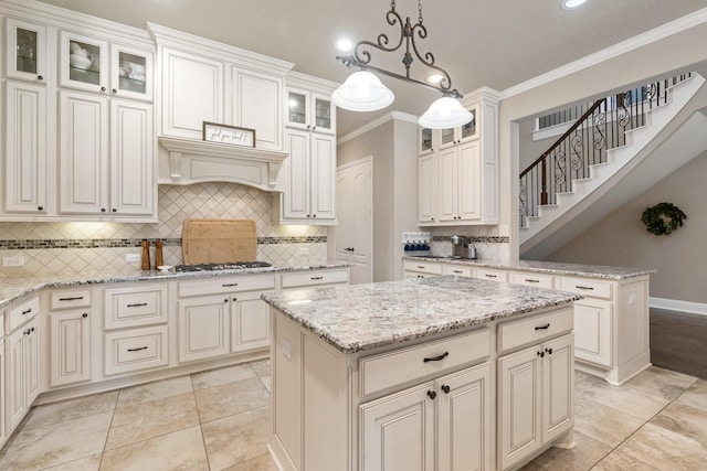 kitchen with a kitchen island, crown molding, light stone countertops, stainless steel gas cooktop, and pendant lighting