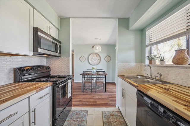 kitchen with a sink, wood counters, black appliances, and white cabinets