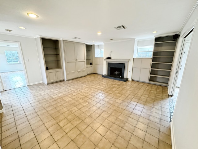 unfurnished living room with a fireplace with raised hearth, a healthy amount of sunlight, built in shelves, and crown molding