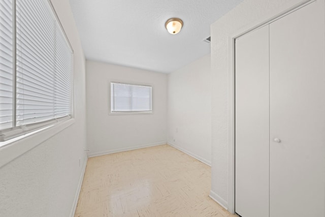 unfurnished bedroom featuring a closet, light floors, a textured ceiling, and baseboards