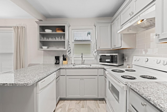 kitchen featuring under cabinet range hood, a sink, tasteful backsplash, white appliances, and a peninsula