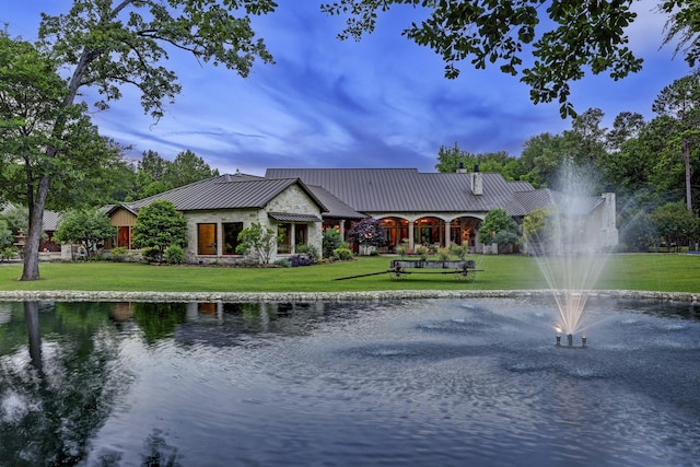 view of front facade with a standing seam roof, metal roof, a front lawn, and a water view