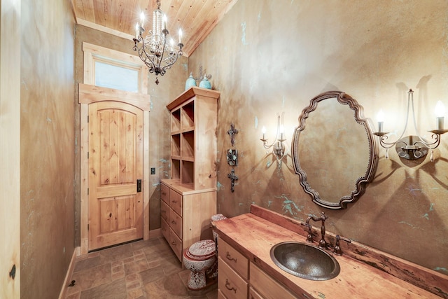 bathroom with vanity, baseboards, stone tile flooring, a notable chandelier, and toilet