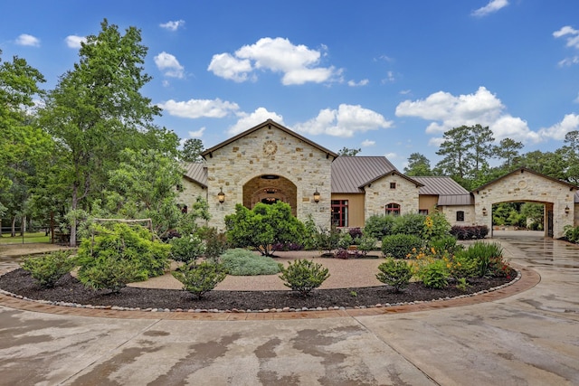 view of front of property with metal roof, stone siding, driveway, and a standing seam roof