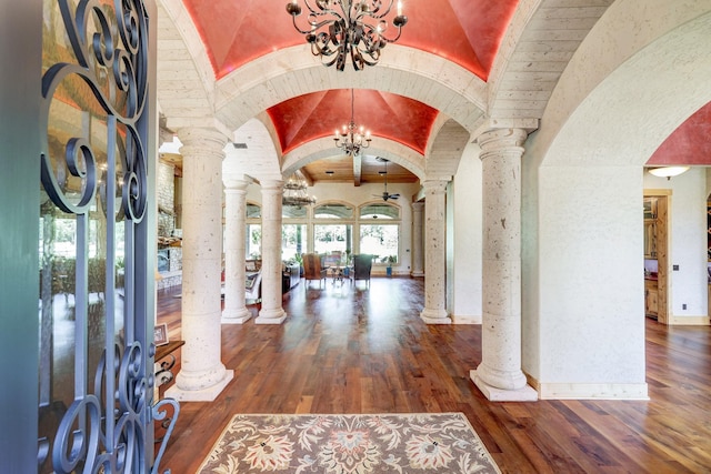 entrance foyer with arched walkways, an inviting chandelier, ornate columns, and hardwood / wood-style flooring