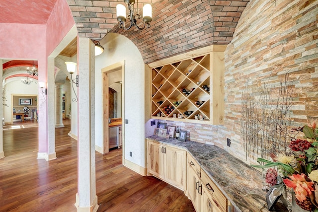 wine area featuring an inviting chandelier, brick ceiling, wood finished floors, and arched walkways