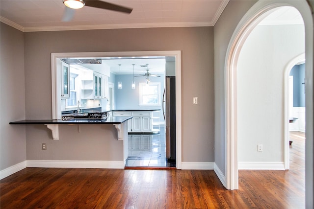 kitchen with a ceiling fan, a kitchen breakfast bar, dark countertops, dark wood finished floors, and freestanding refrigerator