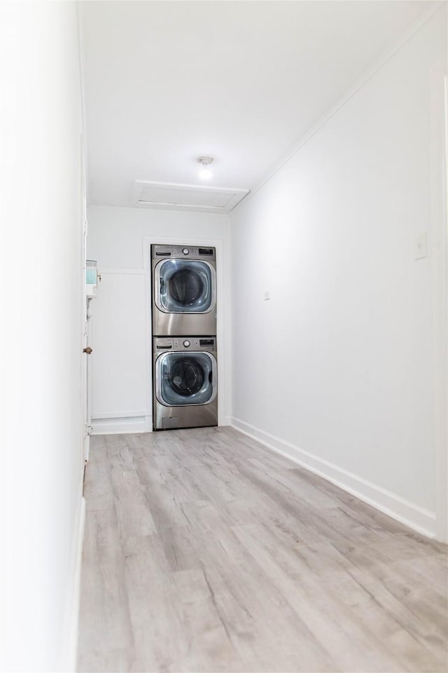 clothes washing area with stacked washer / dryer, laundry area, baseboards, and wood finished floors