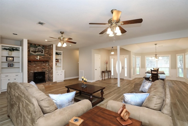 living room featuring visible vents, baseboards, built in features, light wood-type flooring, and a fireplace