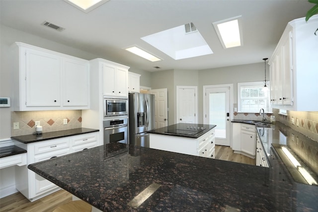 kitchen featuring visible vents, a sink, a center island, appliances with stainless steel finishes, and decorative backsplash