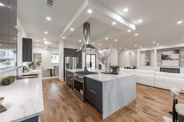 kitchen with visible vents, island range hood, modern cabinets, high end appliances, and a sink