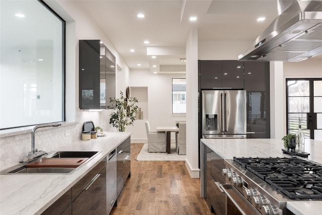 kitchen with modern cabinets, a sink, backsplash, appliances with stainless steel finishes, and wall chimney range hood