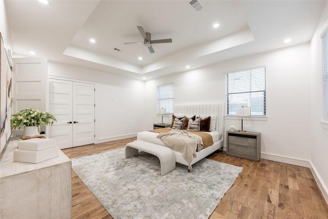 bedroom with a tray ceiling, light wood-style flooring, multiple windows, and visible vents