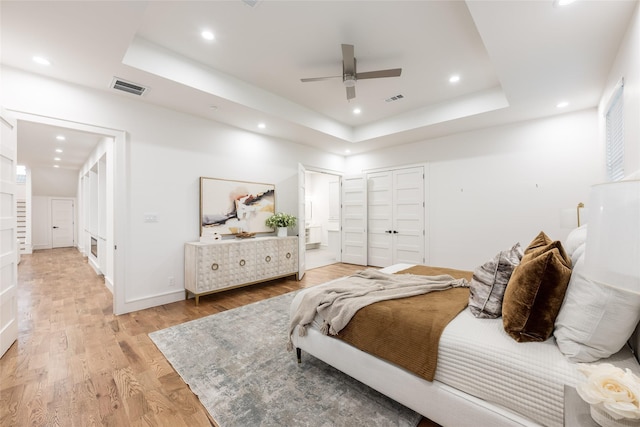 bedroom featuring a raised ceiling, light wood-style flooring, and visible vents