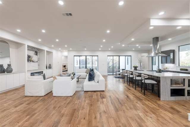 living room with light wood finished floors, visible vents, recessed lighting, and a glass covered fireplace